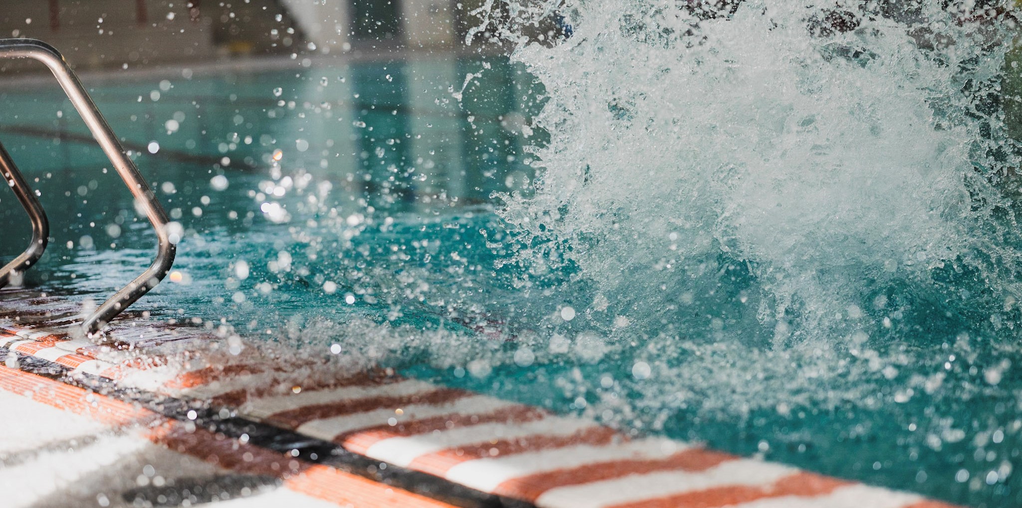 Foto zeigt Beckenrand im Schwimmbad, Wasser spritzt hoch